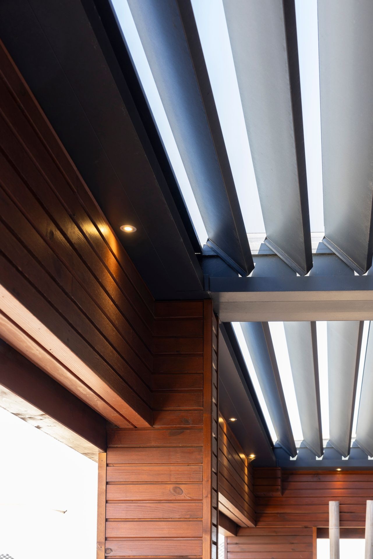 Modern ceiling with wooden panels and exposed metal beams, featuring recessed lighting.