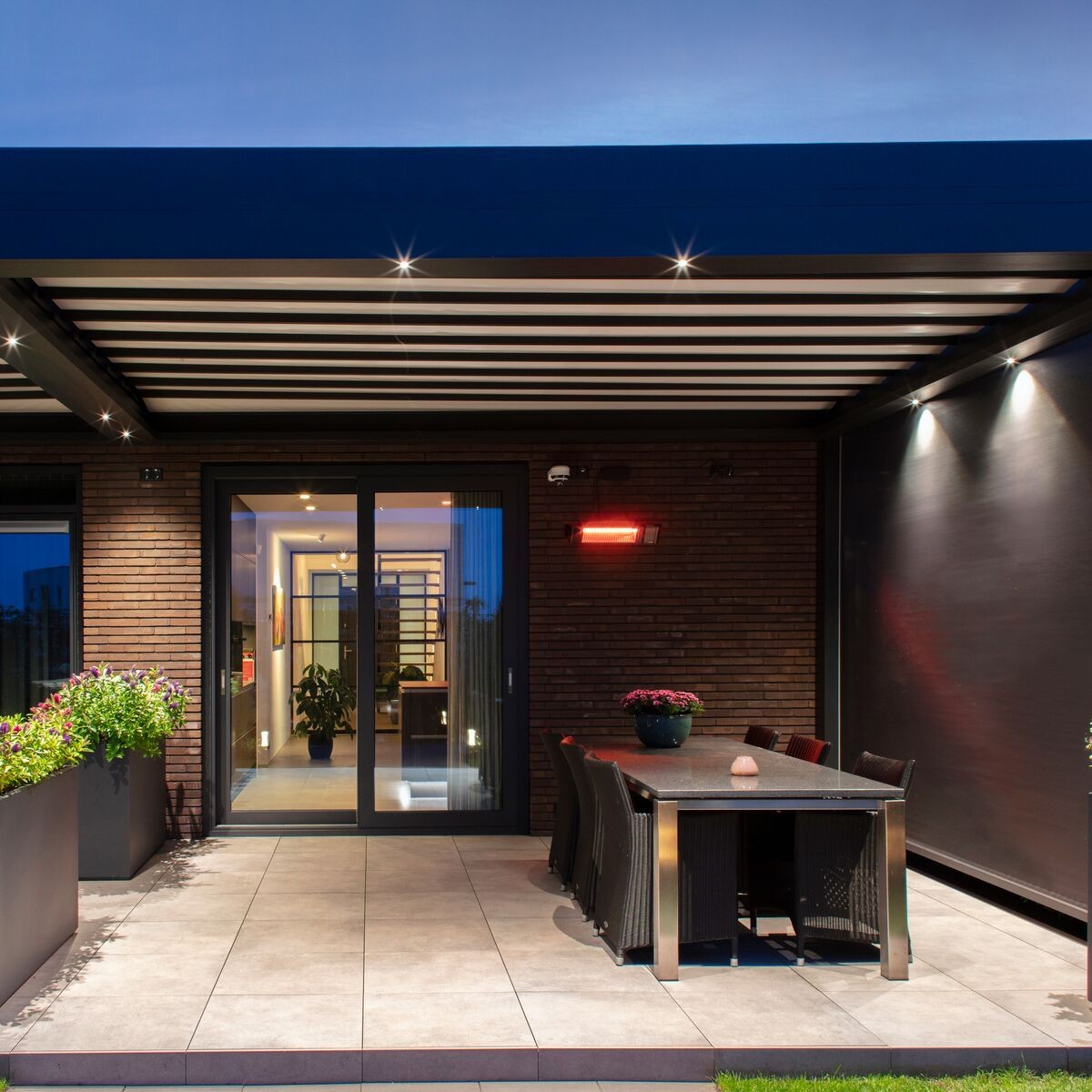 Modern patio with covered seating area, table, chairs, and sliding glass doors at dusk.