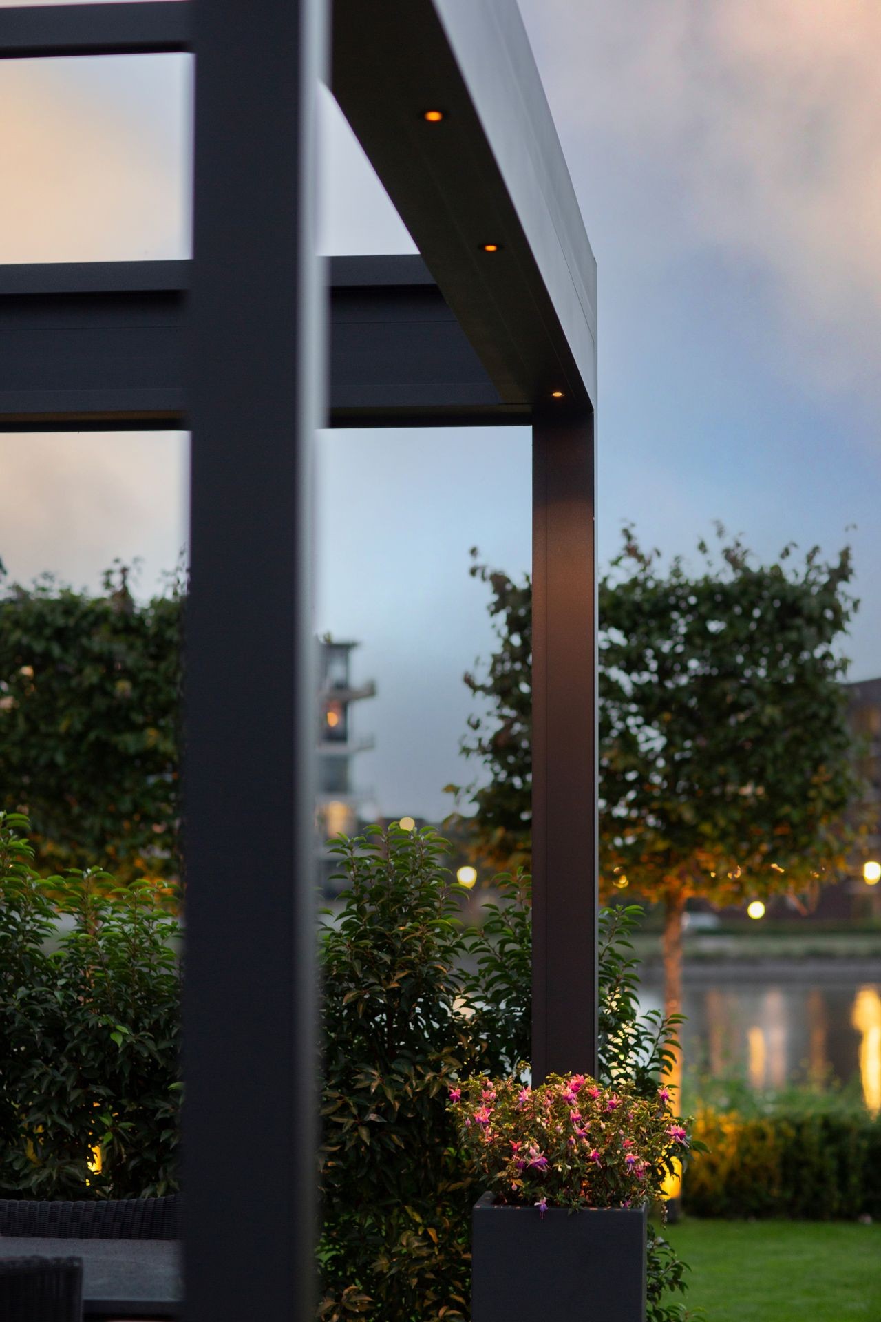 Modern outdoor structure with plants and evening lights in a garden setting.