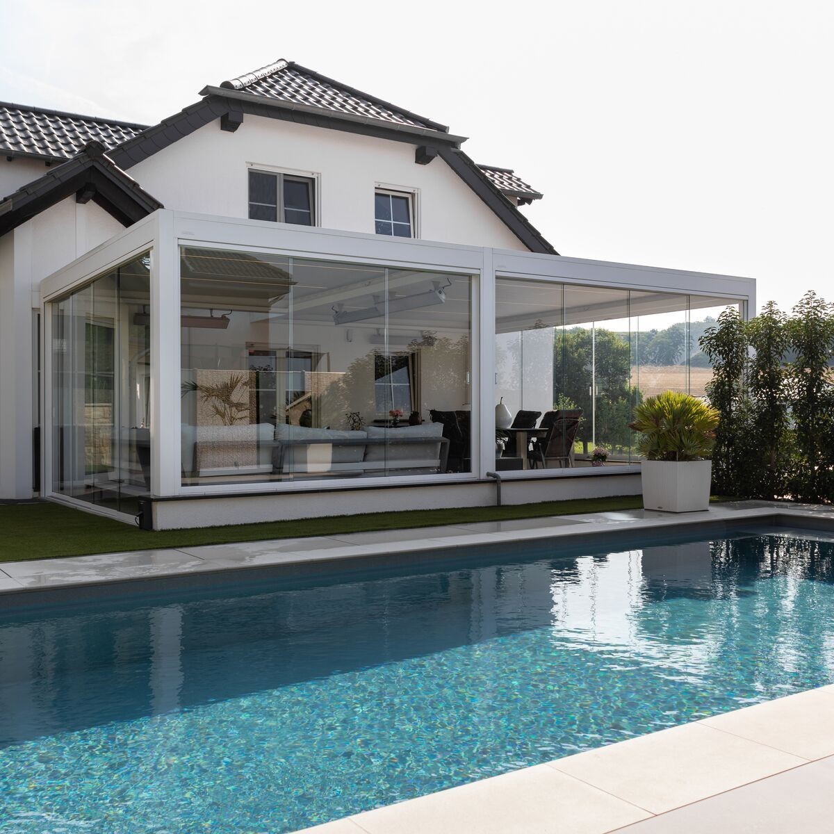 Modern house with large glass-enclosed patio area overlooking a swimming pool with clear blue water.