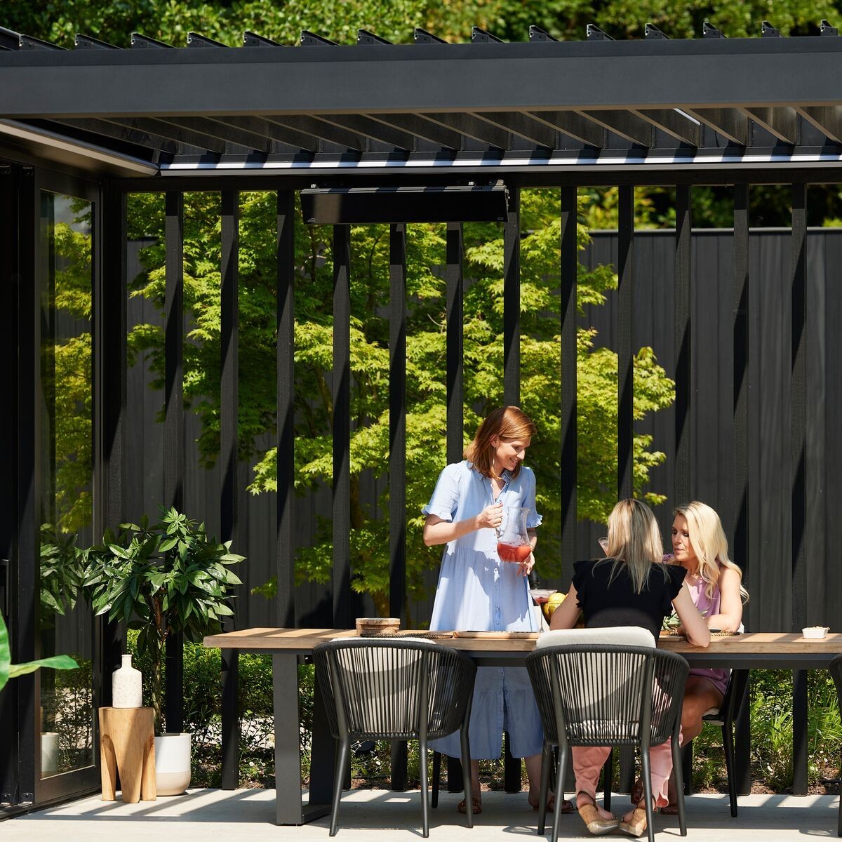 Outdoor dining area with a wooden table and chairs, surrounded by modern architecture and green plants.