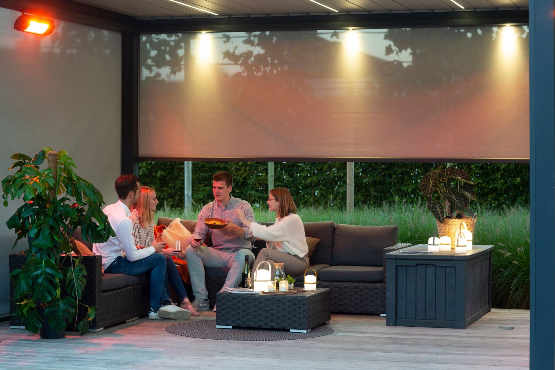 Four people sitting on an outdoor patio, enjoying snacks and drinks near ambient lanterns.