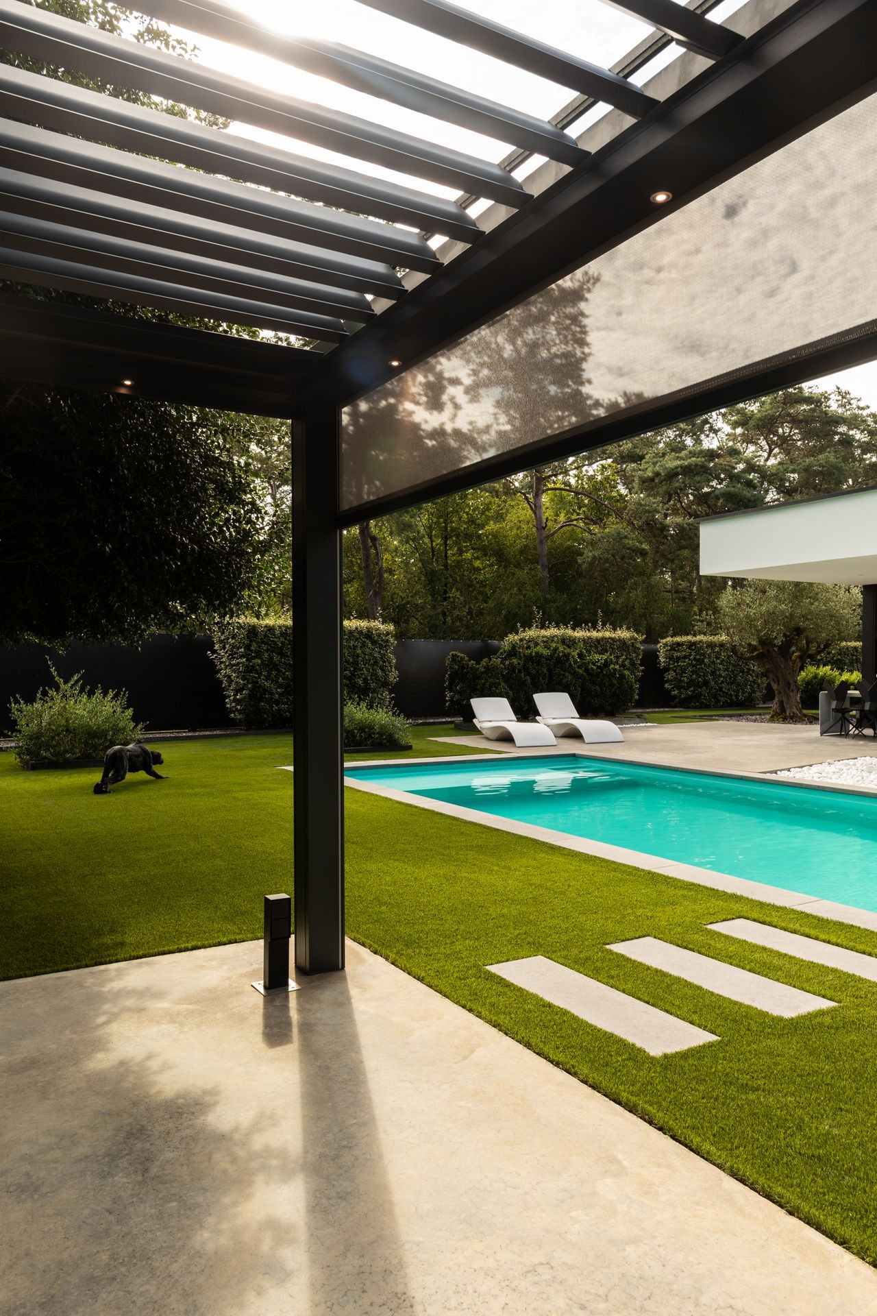 Modern patio overlooking a pool with lounge chairs on a sunny day.