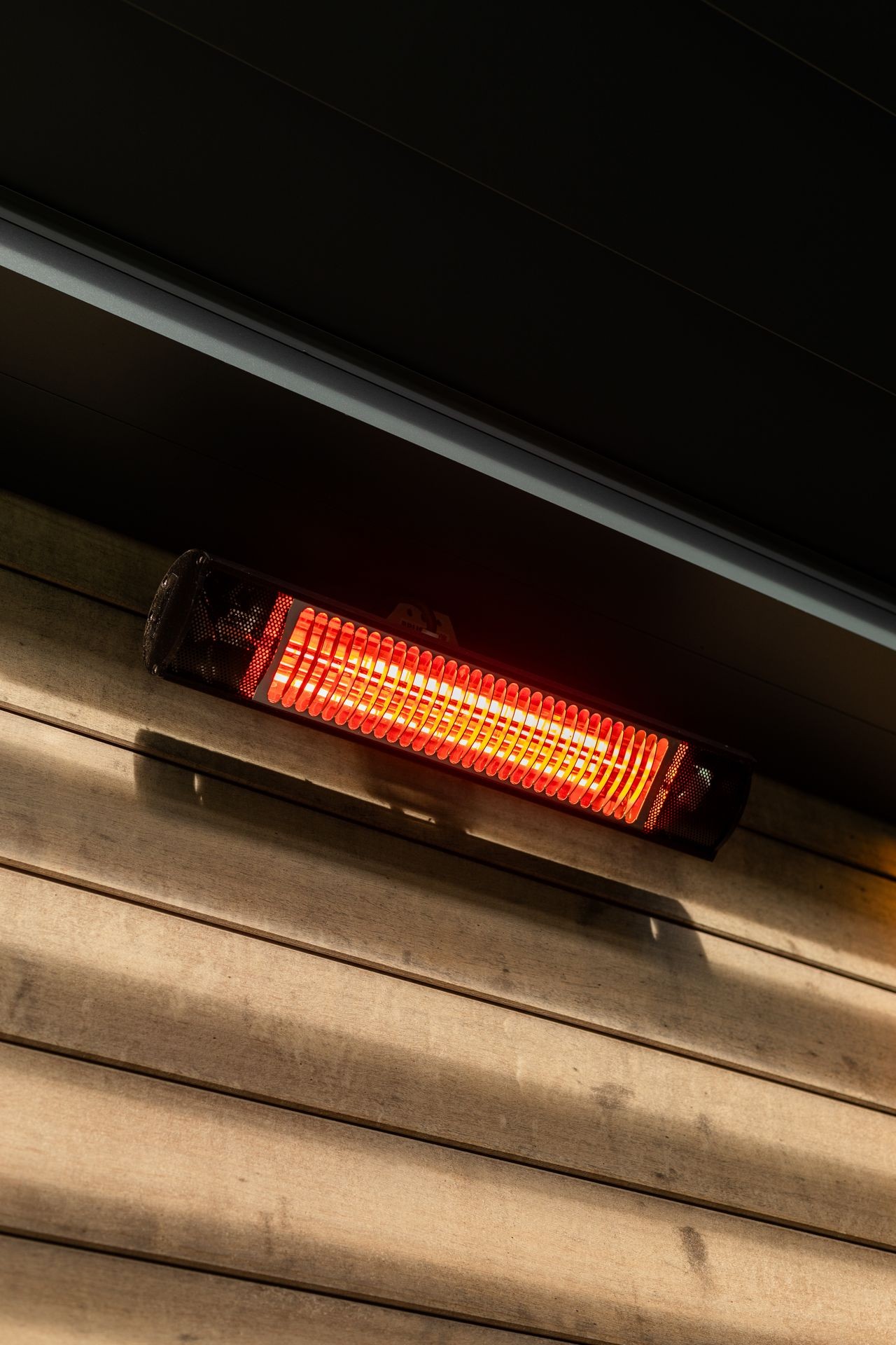 Wall-mounted infrared heater glowing red against a wooden background.